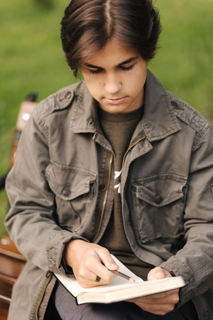 Knappe tiener schildert iets in zijn notitieblok tijdens de pauze, getalenteerde jonge jongen