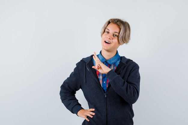 Knappe tienerjongen die V-teken in overhemd, hoodie, vooraanzicht toont.