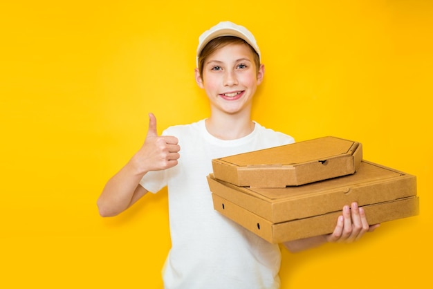 Knappe tienerjongen met een stapel pizzadozen op een gele achtergrond Werk in kindertijdconcept
