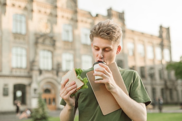 Knappe universiteitsstudent die smakelijke sandwich eet