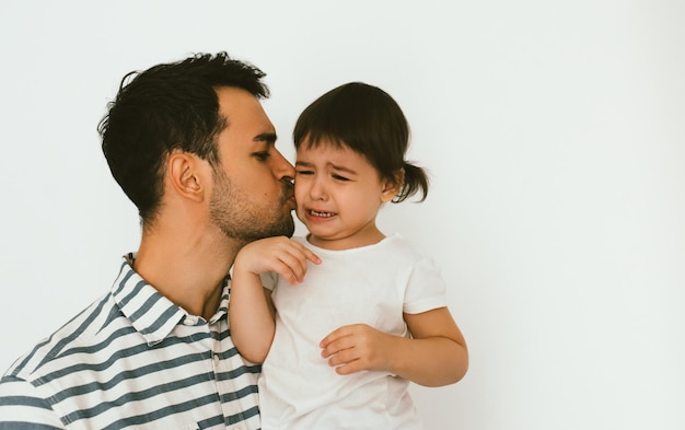 Knappe vader die zijn huilende dochter vasthoudt en kust jonge vader omhelst zijn verdrietig kind aantrekkelijke man ondersteunt zijn ongelukkig peutermeisje jeugd- en vaderschapsrelatie lifestyle familie