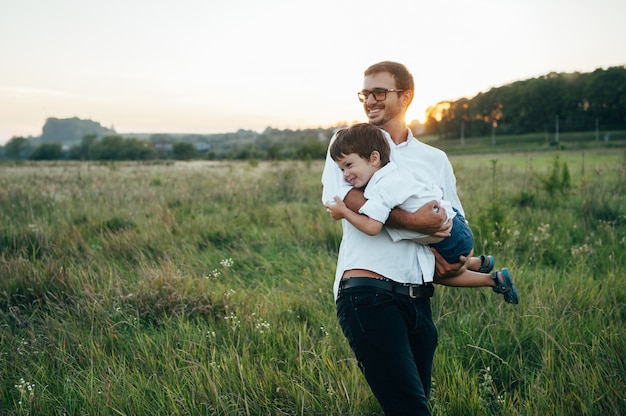 Knappe vader met zijn kleine schattige zoon hebben plezier en spelen op groen grasveld.