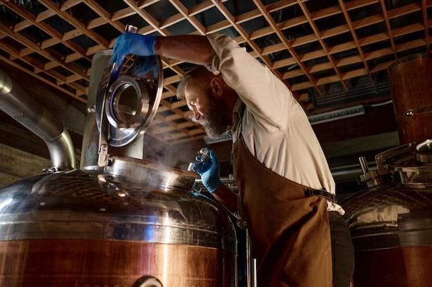 Knappe volwassen brouwer die het proces van het brouwen van bier met stoom inspecteert. Kleine brouwerijfabriek, familiebedrijf concept