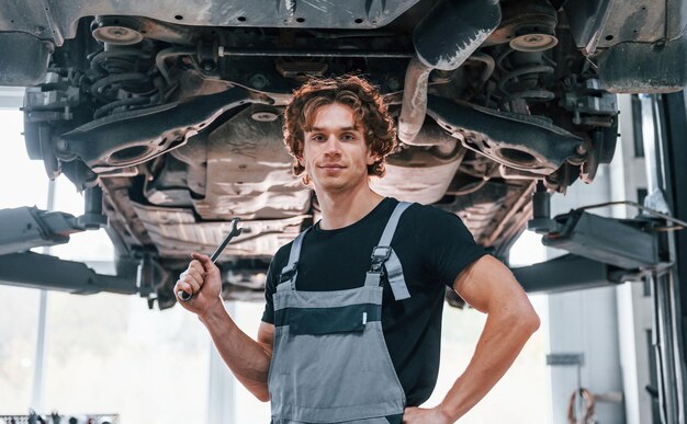 Knappe volwassen man in grijs gekleurd uniform die onder de auto staat