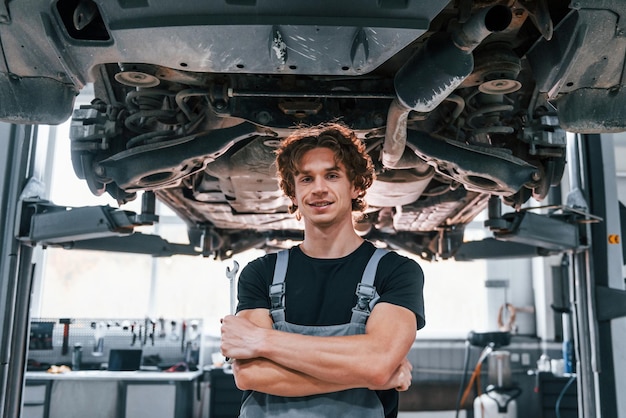 Knappe volwassen man in grijs gekleurd uniform die onder de auto staat