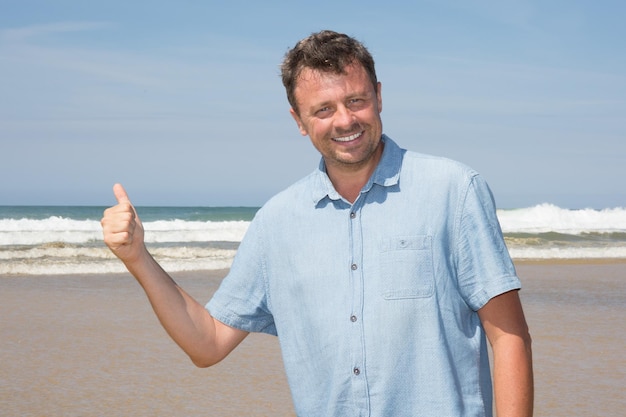 Knappe volwassen man op een strand duim omhoog