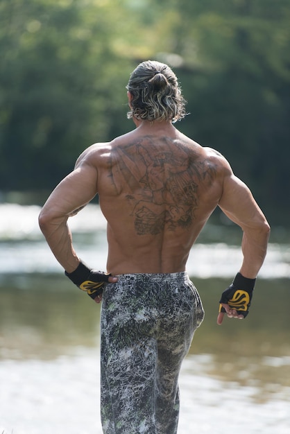 Knappe volwassen Man permanent sterk buiten In de natuur en buigen spieren gespierde atletische Bodybuilder Fitness Model poseren na oefeningen