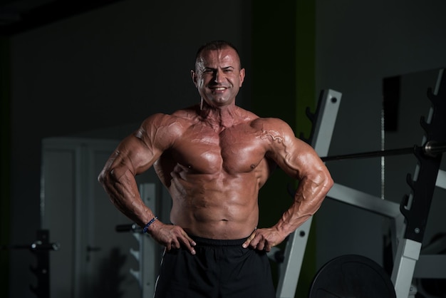 Knappe volwassen man staat sterk in de sportschool en buigt spieren Gespierde atletische bodybuilder Fitness man poseren na oefeningen