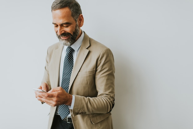 Knappe volwassen zakenman met behulp van mobiele telefoon op kantoor