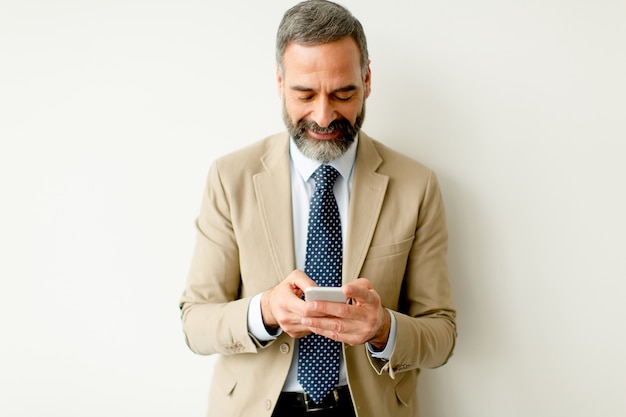 Knappe volwassen zakenman met behulp van mobiele telefoon op kantoor
