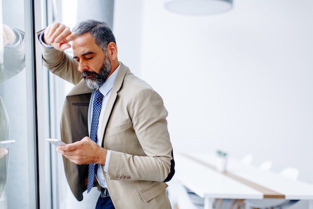 Knappe volwassen zakenman met mobiele telefoon op kantoor