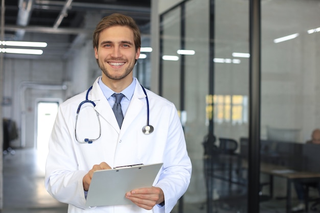 Knappe vriendelijke jonge dokter op ziekenhuis gang kijken camera, glimlachend.