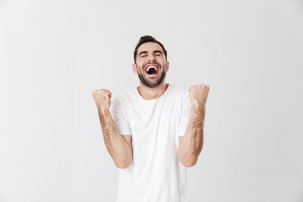 Knappe vrolijke man met een leeg t-shirt dat geïsoleerd over een witte muur staat en succes viert