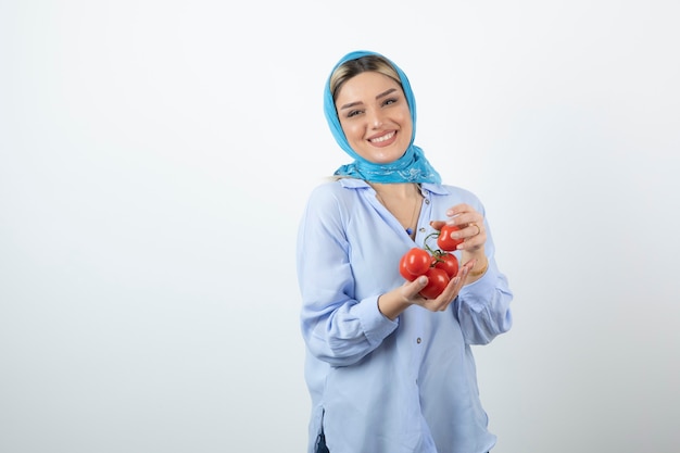 Knappe vrouw die in blauwe sjaal rode verse tomaten houdt