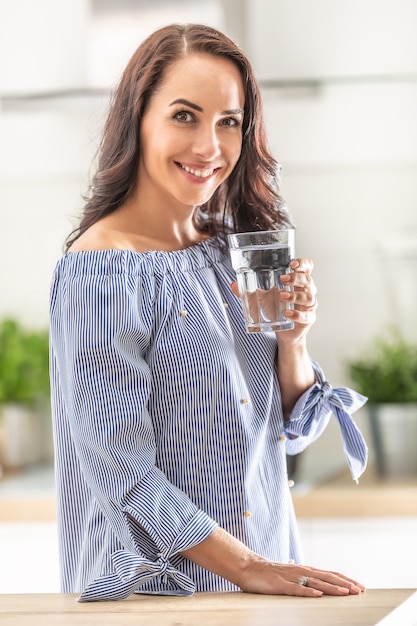 Knappe vrouw drinkt een glas zuiver water in huis.