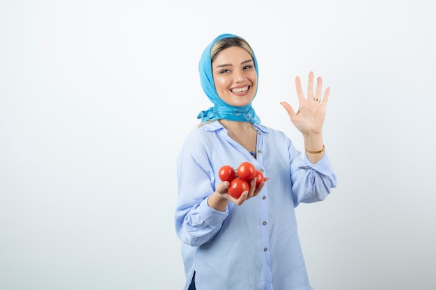 Knappe vrouw in blauwe sjaal die nummer vijf met hand toont en rode tomaten houdt