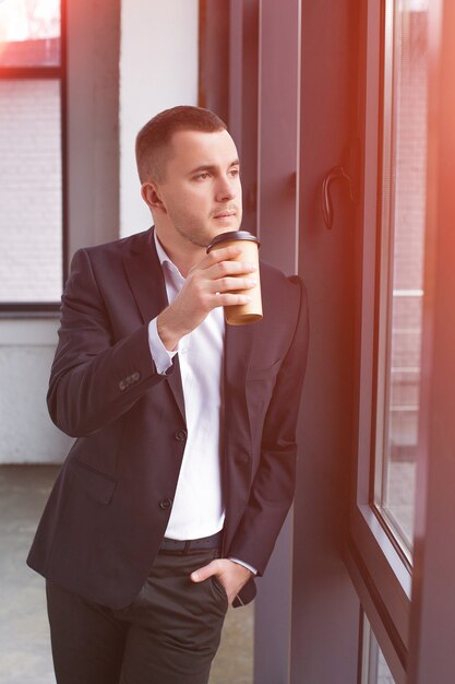 Foto knappe zakenman die een zwart kostuum met een koffiekop draagt