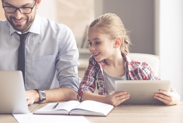 Knappe zakenman en zijn schattige dochtertje gebruiken gadgets en glimlachen terwijl ze samen tijd doorbrengen