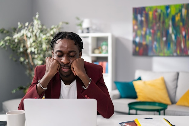 Knappe zakenman in kastanjebruin jasje zit moe voor de koffiemok van het laptopscherm naast hem