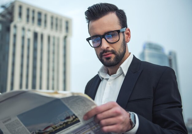 Knappe zakenman in pak en bril leest de krant terwijl hij op het balkon staat