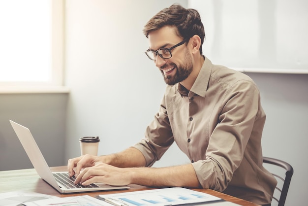 Knappe zakenman lacht terwijl hij met een laptop op kantoor werkt