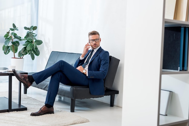 Foto knappe zakenman met een bril die op de bank zit en met een smartphone praat