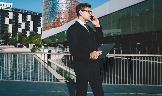 Knappe zakenman met gadget die op telefoon spreekt