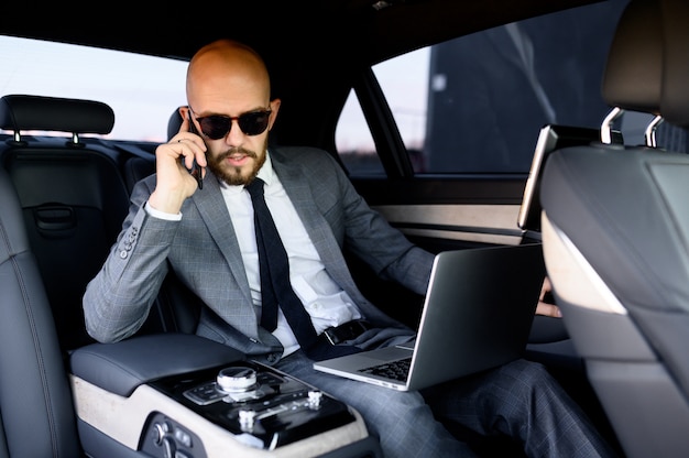 Knappe zakenmanzitting met laptop op de achterbank van de auto