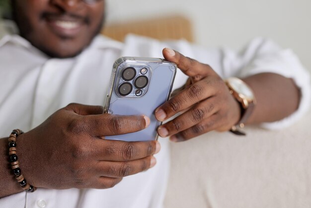 Knappe zwarte Afro-Amerikaanse man die smartphone gebruikt terwijl hij op een bank zit in een gezellige woonkamer