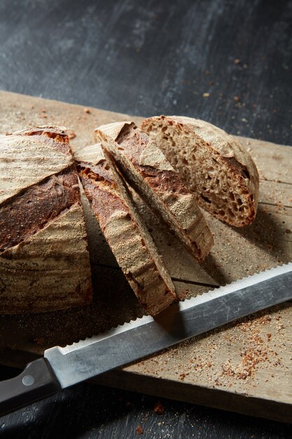 Knapperig brood wordt gesneden op een oude houten snijplank op een donkere achtergrond