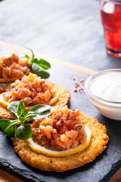 Knapperige aardappelpannenkoekjes met zalm en zure room. Draniki met zalm op een zwarte steen