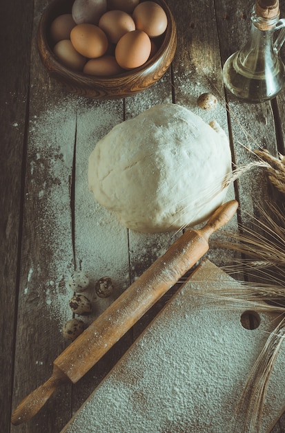 Kneaded dough, ears of wheat,rolling pin, eggs and a bottle of oil on the old rustic table closeup