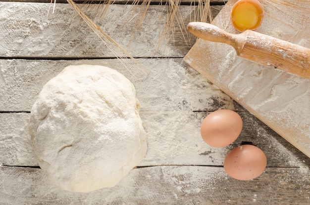 Kneaded dough ears of wheatrolling pin eggs and a bottle of oil on the old rustic table closeup