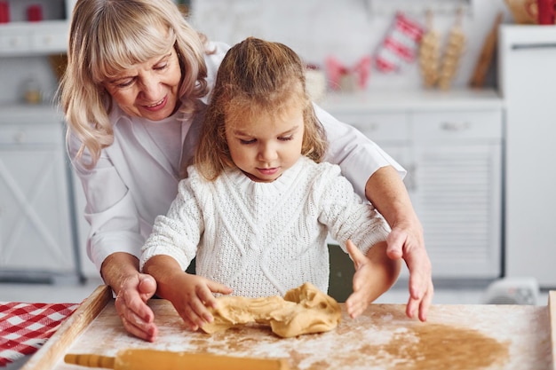 小さな孫娘と一緒に生地の先輩の祖母をこねて、キッチンでクリスマスのお菓子を作ります