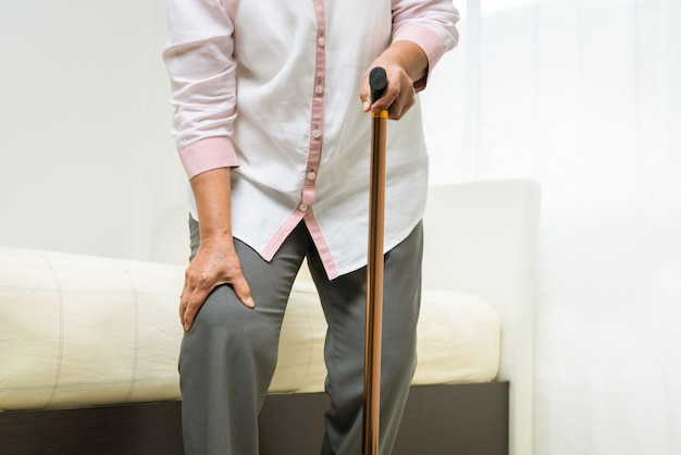 Foto dolore al ginocchio della donna senior con il bastone, problema di sanità del concetto senior