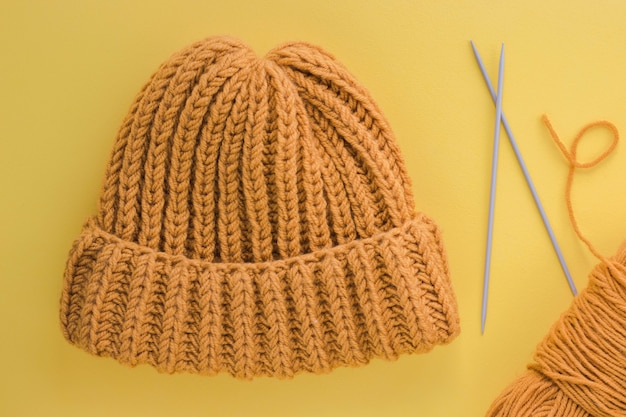 Knetted yellow hat with metal needles and threads isolated on yellow background