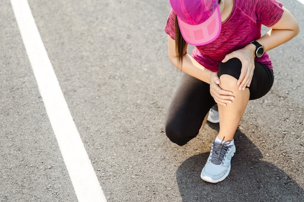 Knieblessures. sport vrouw met sterke atletische benen met knie met haar handen in pijn na het lijden van spierblessure tijdens een running training training op de atletiekbaan. gezondheidszorg en sport concept.