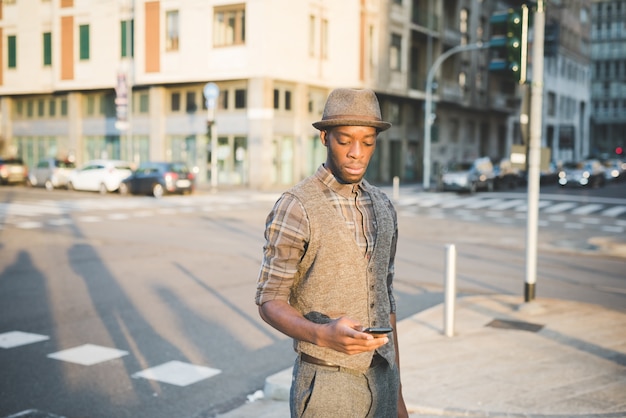 Kniefiguur van de jonge knappe afro zwarte mens in stadszonsondergang die een smartphone houden