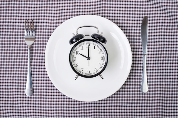 사진 나이프와 포크 식탁보 배경에 흰색 접시에 알람 시계.