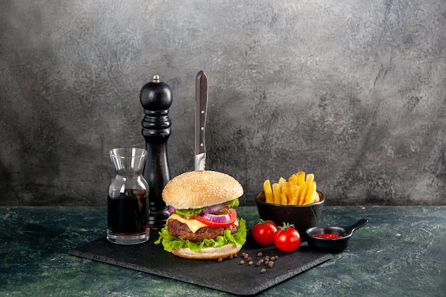 Knife in delicious meat sandwich and green pepper on black tray sauce ketchup tomatoes with stem fries on isolated dark surface