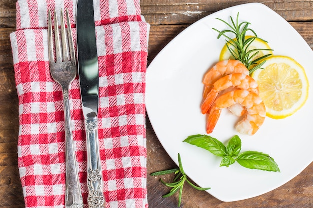 Knife and fork next to a dish with cooked shrimps