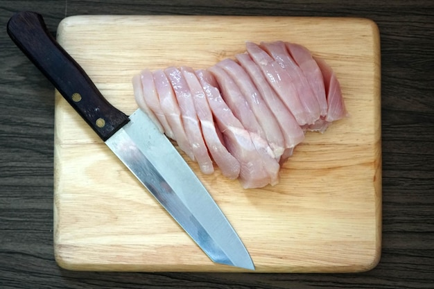 Knife and fresh chicken slice on a wooden chopping board