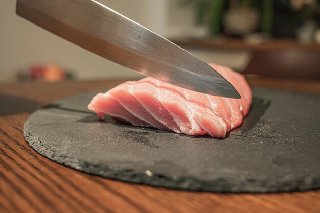 A knife is cutting a piece of sushi on a black plate.