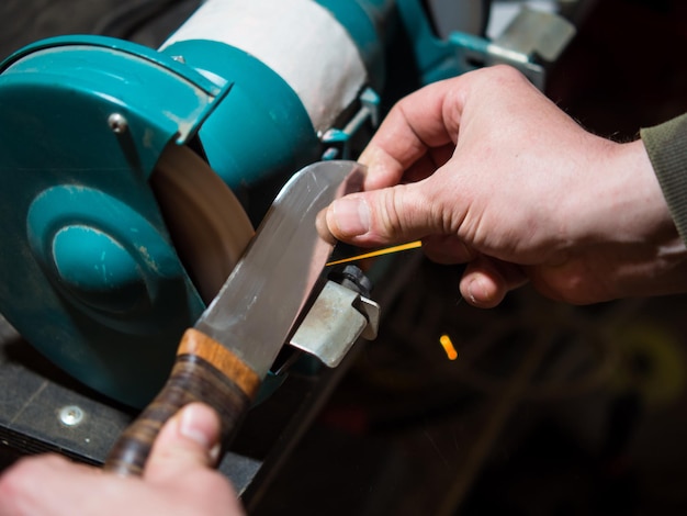 Knife sharpener and a hand with a blade a man sharpens a knife on a grinder