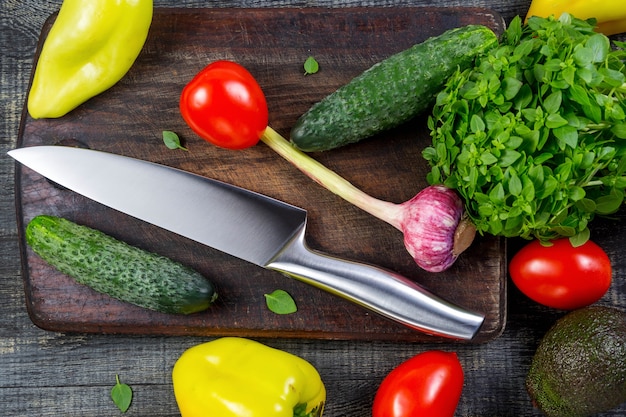 Knife and Wooden Cutting Board Surrounded by Fresh Herbs and Assortment of Raw Vegetables