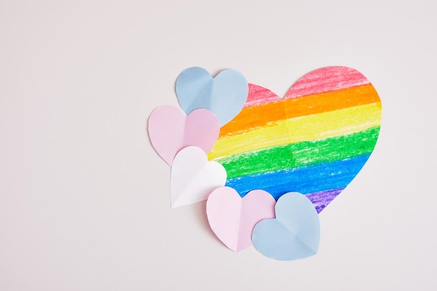 Knip gekleurde papieren harten uit op grijze achtergrond, transseksuele kleuren, lgbt-trotsconcept, grote regendruppelkleuren hart tekenen met krijt