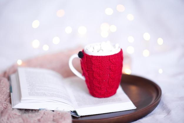 Knited cup of coffee on open book over Christmas lights close up Good morning