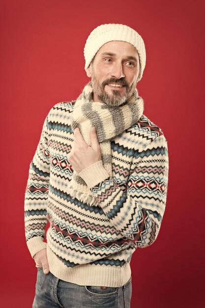 Knitted accessories Winter weather style Menswear concept Fashion collection Fashion clothes Cold winter conditions Handsome bearded man wearing hat and scarf red background Winter fashion