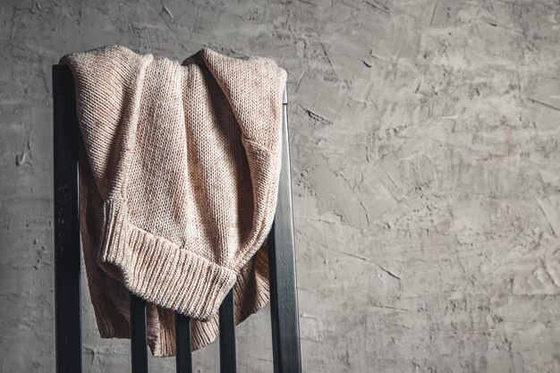 Knitted beige sweater on the back of a white wooden chair