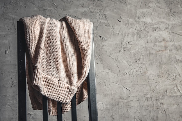 Knitted beige sweater on the back of a white wooden chair